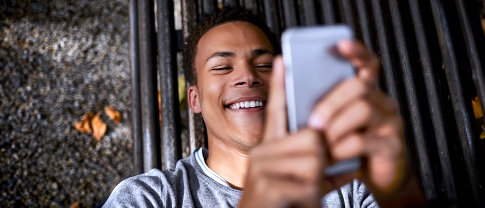 A man smiling at his phone, asking a girl out over text