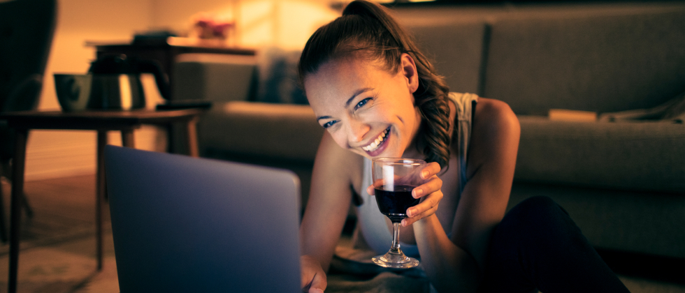 A woman sitting in front of a laptop, doing a long distance date idea with her partner.