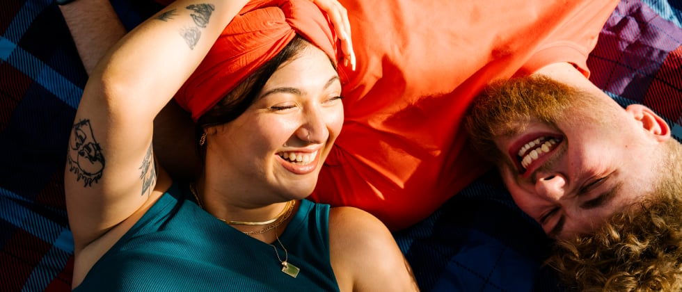 A woman is lying with her head on a man's chest, both smiling at each other