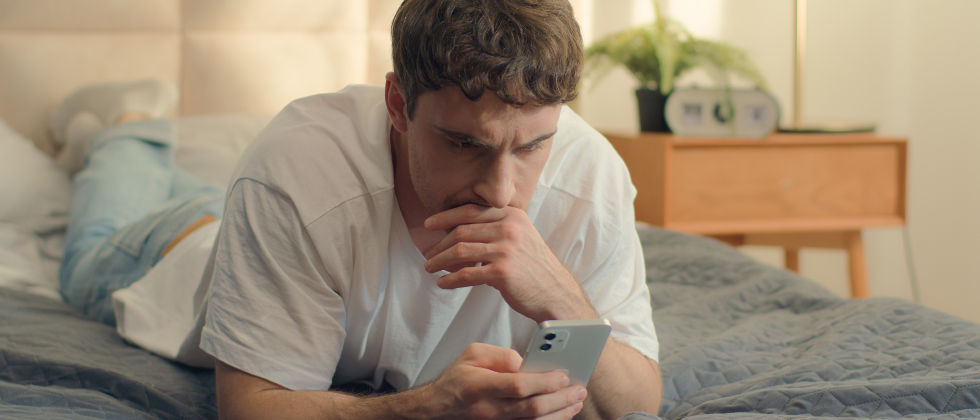 A guy looking at his phone, wondering how to text a girl for the first time