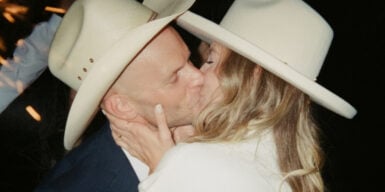A woman and a man with cowboy hats on are kissing each other passionately.