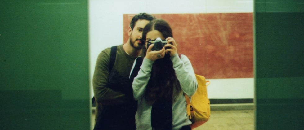 A man and a woman standing next to each other, photographing themselves in the mirror.