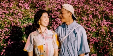 A woman and a man standing next to each other in front of flowers. They smile at each other and seem to be attracted to each other.