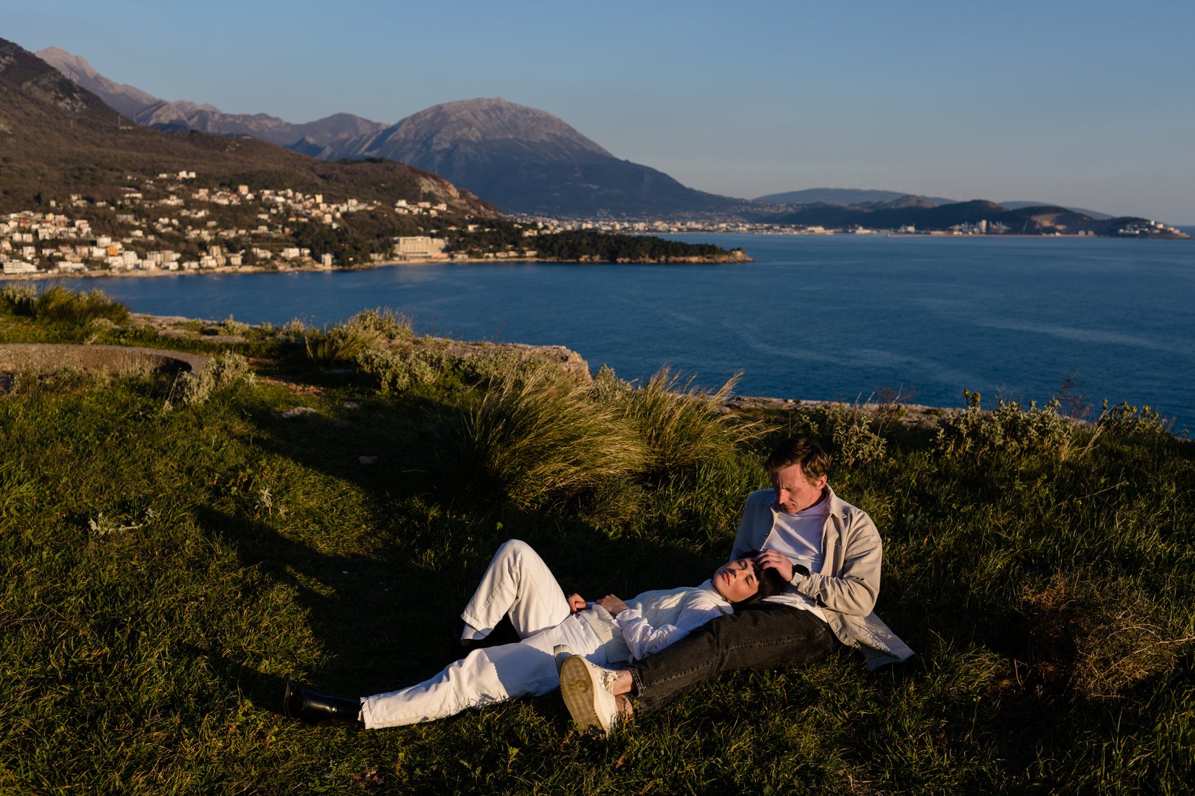 Young spouses rest in the grass on the hill above the Adriatic sea in the evening