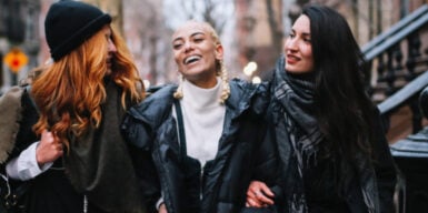 Three women walk together through the city arm in arm as a symbol of Polymory