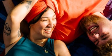 A woman is lying with her head on a man's chest, both smiling at each other