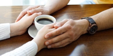 A woman holding her coffee with her boyfriend's hands around hers