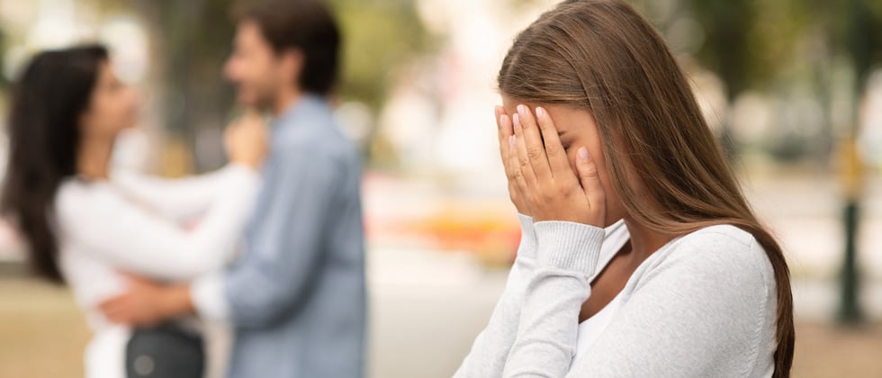 A woman crying in her hands with a couple about to kiss in the background