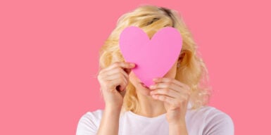 A woman holding a pink cutout heart over her face