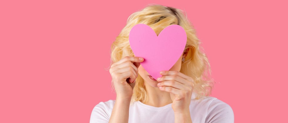 A woman holding a pink cutout heart over her face