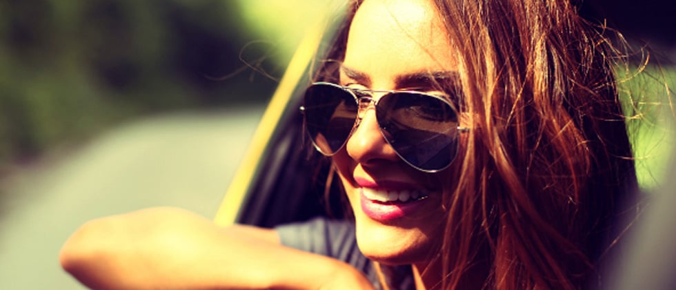 A woman in a car with sunglasses smiling while her head is out the window