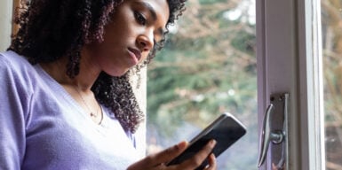 A woman standing at the door looking solemnly into her phone