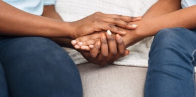 A couple holding hands on the couch in a comforting way