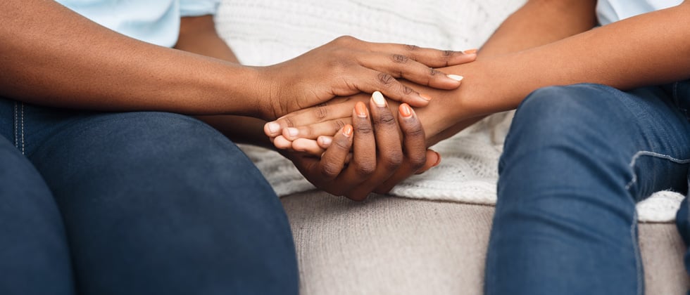 A couple holding hands on the couch in a comforting way